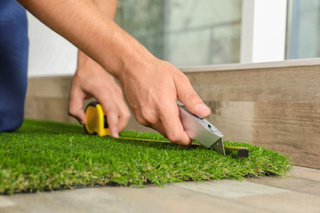 Man cutting artificial grass carpet indoors, closeup