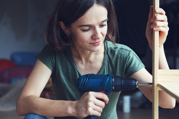 pretty young woman holding screwdriver and repairing or making wooden furniture