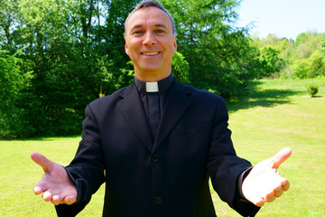 A good looking catholic priest is welcoming us in joy. He looks at us with optimism, openning his arms in peace.