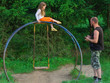 © SVIATLANA - A father watches his daughter's safety on an old, vintage, retro, vintage playground. The girl climbed high to the top of the old swing in the form of an arc.