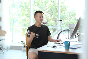 Canvas Print - Young man lifting weights and using computer in office. Workplace fitness