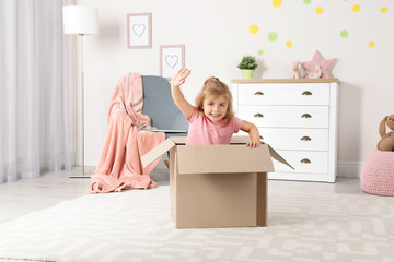 Wall Mural - Cute little girl playing with cardboard box at home