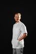 © Ирина Щукина - Handsome mature male surgeon with hand in pocket on black background. Smiling doctor man in surgery suit.
