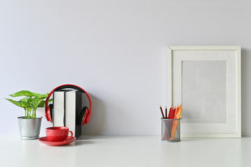 Office stuff with books, coffee, colour pencil, photo frame, headphones and plant on workspace table.