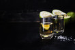 Golden tequila shots with sea salt, juicy lime on vintage black wooden board, toned, selective focus, copy space.
