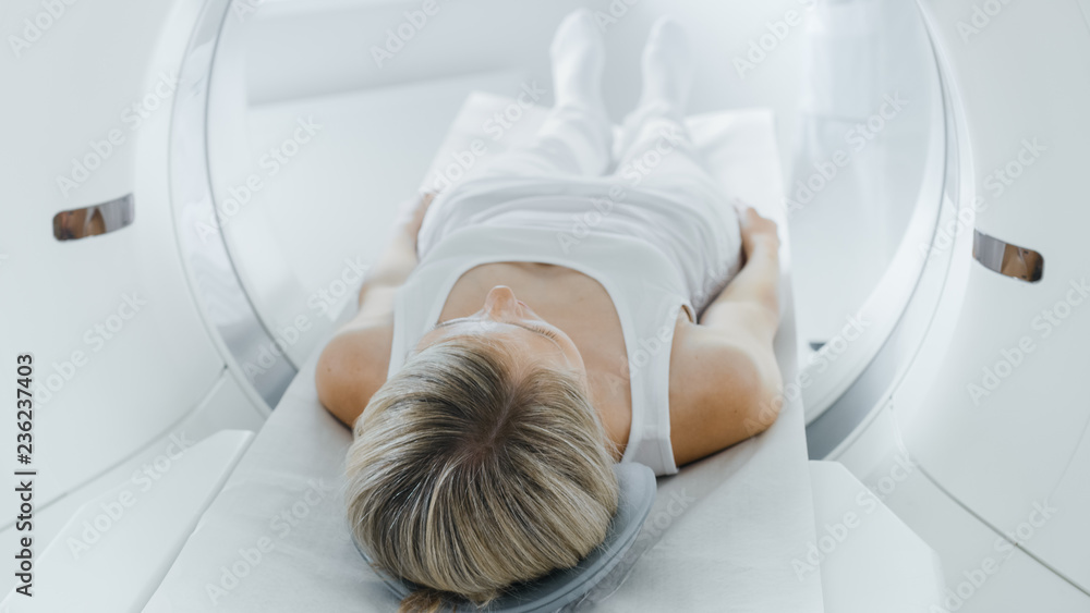 Female Patient Lying on a CT or MRI Scan, Bed is Moving inside Machine Scanning Her Body and Brain. In Medical Laboratory with High-Tech Equipment. - obrazy, fototapety, plakaty 
