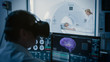 © Gorodenkoff - Futuristic Concept: In Medical Control Room Doctor Wearing Virtual Reality Headset Monitors Patient Undergoing MRI or CT Scan Procedure. Computer Displays Show 3D Brain Model with Possible Cancer.