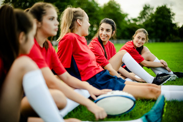 Wall Mural - Happy female rugby players sitting on the grass