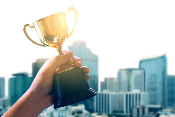 Wall Mural - trophy on winner hand with blur background business tower and sun flare on the sky