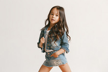 Full Length Portrait Of Cute Little Kid Girl In Stylish Jeans Clothes Looking At Camera And Smiling, Standing Against White Studio Wall. Kids Fashion Concept