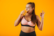 © Drobot Dean - Image of pretty chubby woman in tracksuit smiling and drinking orange juice, isolated over yellow background