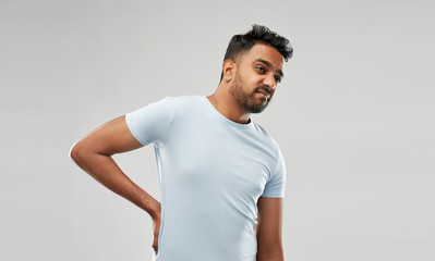 health problem and people concept - unhappy indian man suffering from pain in back or reins over grey background