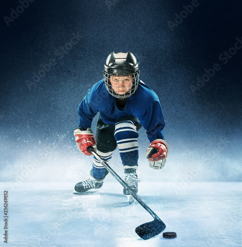 Fototapety Hokej  maly-chlopiec-gra-w-hokeja-na-arenie-hokeista-w-mundurze-ze-sprzetem-nad-niebieskim