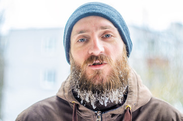 Young man with a beard covered with icicles and frozen droplets on the street after exercise. The concept of outdoor sports in the winter. Winter street portrait. Endurance concept