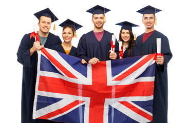 Wall Mural - education, graduation and people concept - group of happy graduate students in mortar boards and bachelor gowns with diplomas and british flag over white background