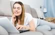 © JackF - Smiling woman is working with laptop lying on sofa
