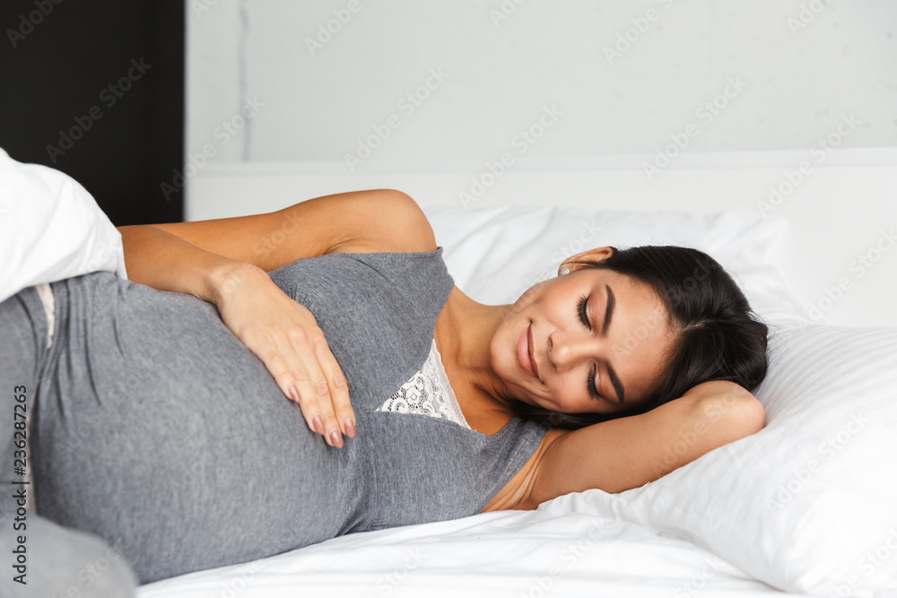Pregnant woman indoors at home lies in bed. - obrazy, fototapety, plakaty 