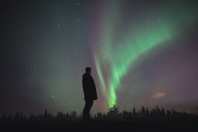 Man Standing And Watching Northern Light / Aurora Borealis In The Sky Of Finland During Winter