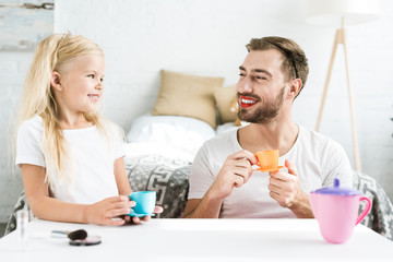 Wall Mural - father with red lipstick and cute happy daughter smiling each other while playing with toy dishes at home