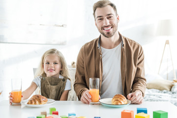 Wall Mural - happy father and cute little daughter smiling at camera while having breakfast together