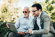 © bnenin - Handsome mature man and young elegant man looking at laptop outdoors.
