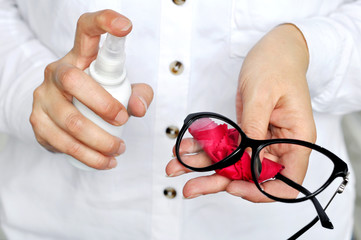 Women hand  holding white spray bottle cleaning trendy black glasses lens with red microfiber tissue.healthcare, vision and medicine concept 