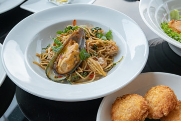 Thai Food. Spicy Spaghetti with Seafood, shrimps, mussel, squid and Thai Herb. close-up on a white plate. Healthy delicious lunch (Thainame : Spaghetti Pad Kee Mao Tha-lay)