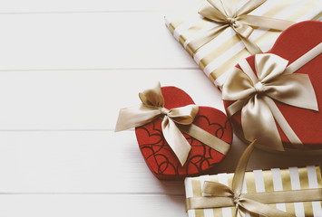 Shape heart gift boxes on a white wooden table. Golden and red gift boxes on a white background.