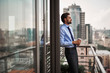 Leinwandbild Motiv Corporate time-out culture. Side on portrait of businessman standing on office balcony with cup of coffee and looking at city view