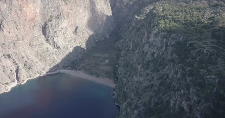 Wall Mural - High altitude aerial drone video tracking left Butterfly Valley beach, waterfront and cliffs extending inland in Oludeniz, Fethiye, Turkey. 4k at 23.97fps
