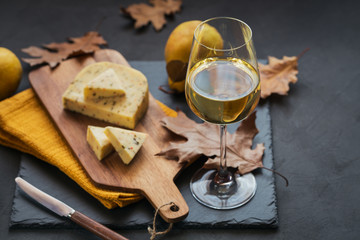 Wall Mural - A glass of white wine served with cheese in a cutting board on dark background