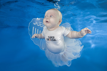 Little funny fairy under water on a blue water background.  Healthy family lifestyle and children water sports activity. Child development, disease prevention