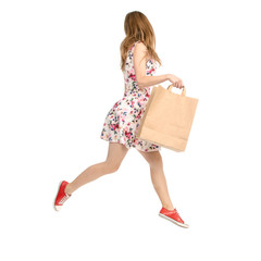 Wall Mural - Beautiful woman in dress with flowers print and sneakers showing of positive emotions runs with bag package  back view on white background isolation