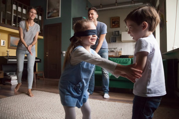 Young large family with two children playing hide-and-seek, little girl with blindfold caught boy, sister and brother playing together, family spending time together