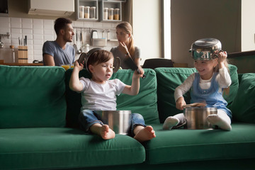 Canvas Print - Happy toddler girl and boy playing with kitchenware on sofa at home, little sister and brother laughing using pots as drums and hats, holding kitchen utensils, making noises, spending time together