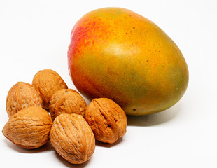 one ripe juicy mango fruit and six inshell walnuts on white background