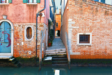 Wall Mural - a glimpse of Venice with the very narrow street in the middle of the old red brick houses overlooking a canal in Venice