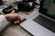 Closeup of laptop keyboard and screen, millennial hipster man with hand tattoo inserts memory card into multifunctional cable adaptor. Creative photographer works with technology and digital media
