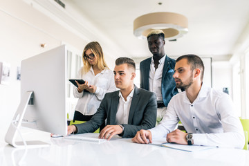 Coworkers looking at a computer and talking about work in modern office.