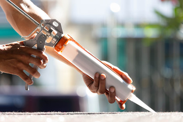 Men's hand uses silicone adhesive with a glue gun to repair worn windows.