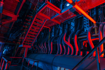 Inside of old abandoned factory. Rusty ruined industrial pipeline connection. Abstract red illuminated industrial background