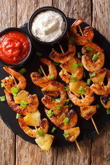 Spicy shrimp kebab with pineapples served with two sauces close-up. Vertical top view