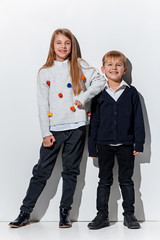 The portrait of cute little kids boy and girl in stylish jeans clothes looking at camera against white studio wall. Kids fashion and happy emotions concept