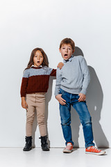 Wall Mural - The portrait of cute little kids boy and girl in stylish jeans clothes looking at camera against white studio wall. Kids fashion and happy emotions concept