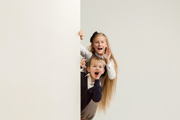 Wall Mural - Banner with a surprised children peeking at the edge with copyspace. The portrait of cute little kids boy and girls looking at camera against white studio wall. Kids fashion and happy emotions concept