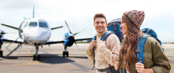 Canvas Print - travel, tourism and people concept - couple of tourists with backpacks over plane on airfield background