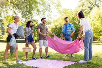 Sticker - friendship and leisure concept - group of happy friends with blanket, pillows and basket arranging place for picnic at summer park