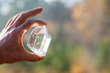 A Hand holding a transparent crystal quartz with the sun hitting the gemstone and a blurry background