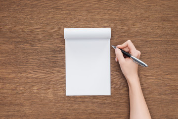 cropped view of person holding pen over blank notebook on wooden background