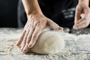 Male chef hands knead dough with flour on kitchen table